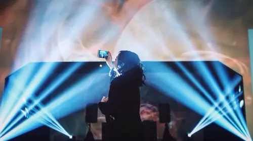 woman reaching over crowd to record stage 